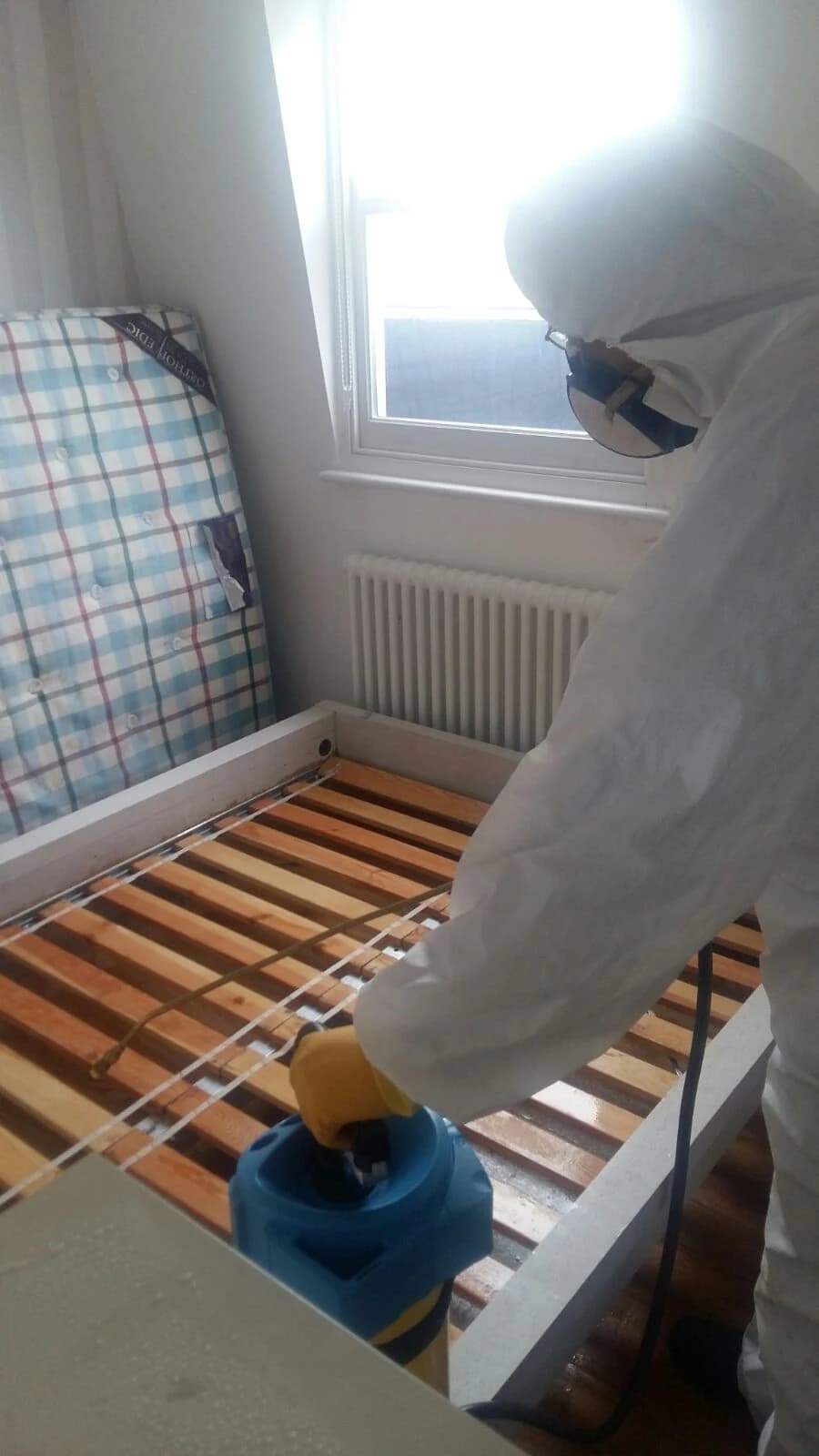 BuzzKill pest control technician in PPE applying insecticide to a bed frame during bed bug treatment